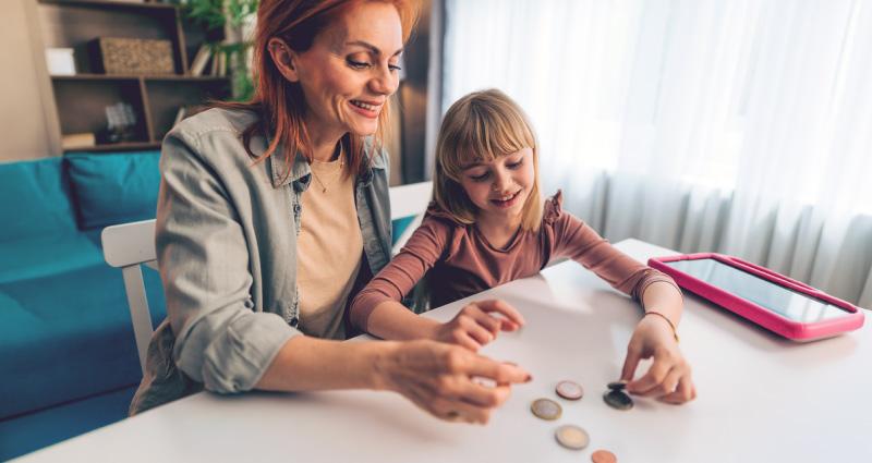 Lapsevanem istub koos lapsega laua taga ja loeb peenraha.
