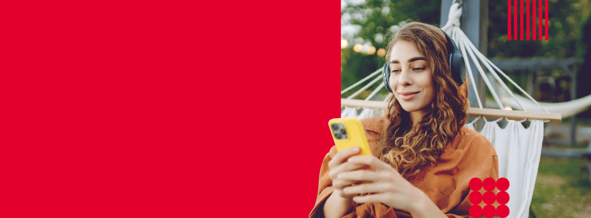 Woman with headphones sitting outside in hammock, checking her phone. 