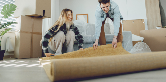 A couple is laying out a carpet in their newly purchased home.