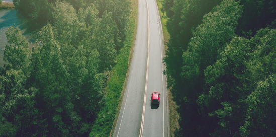 Ceļs starp mežu par kuru brauc auto