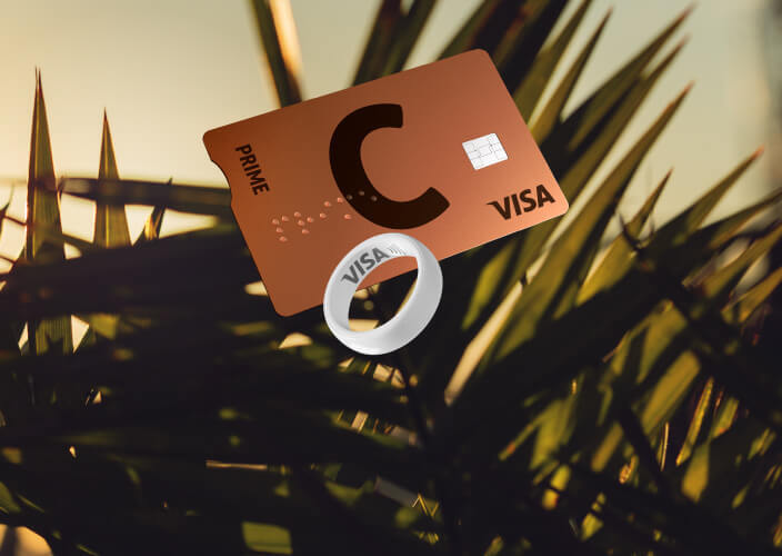 C prime lava VISA card and white payment ring with VISA logo against palm leaves at sunset.