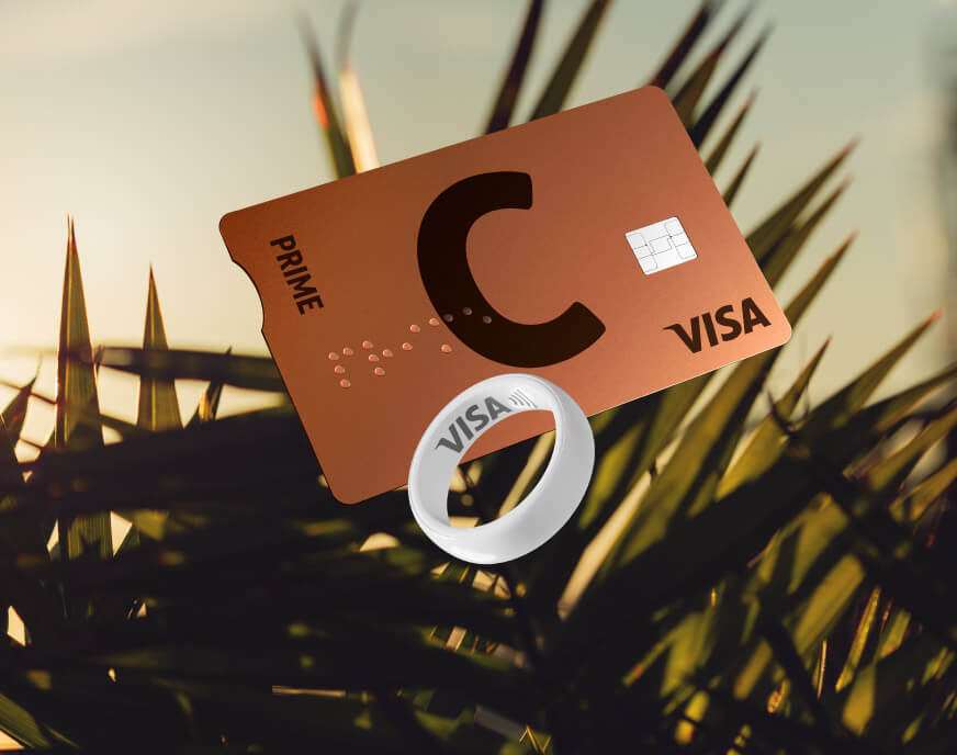 C prime lava VISA card and white payment ring with VISA logo against palm leaves at sunset.