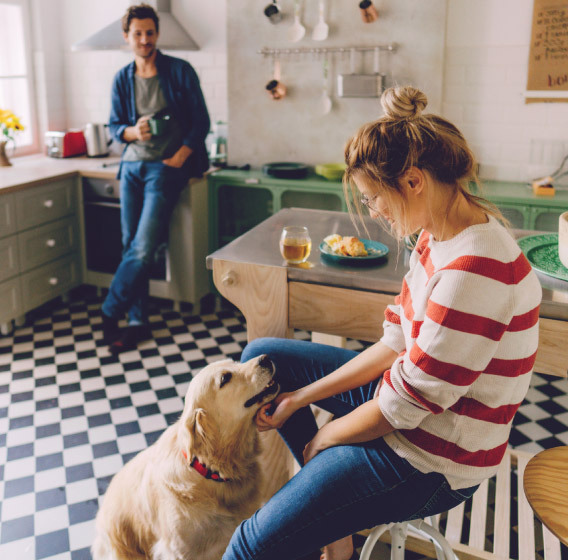 Man and woman relaxing in their kitchen playing with their dog. 
